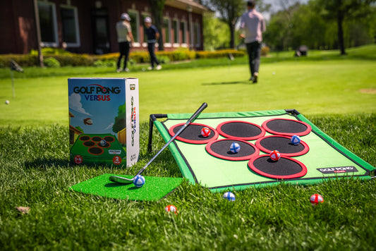 Golf Pong Versus set with two velcro target mats, hitting mat, and foam balls set up on a lawn with players in the background, one of the best lawn games for adults